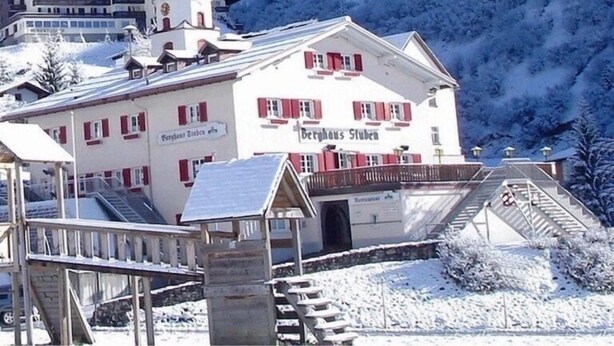 A hotel with a red and white facade, a bell tower, and a sign reading "Berghaus Stuben".
