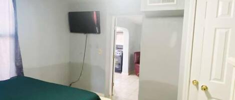 Une pièce avec un lit, un ventilateur de plafond, une télévision et une porte.