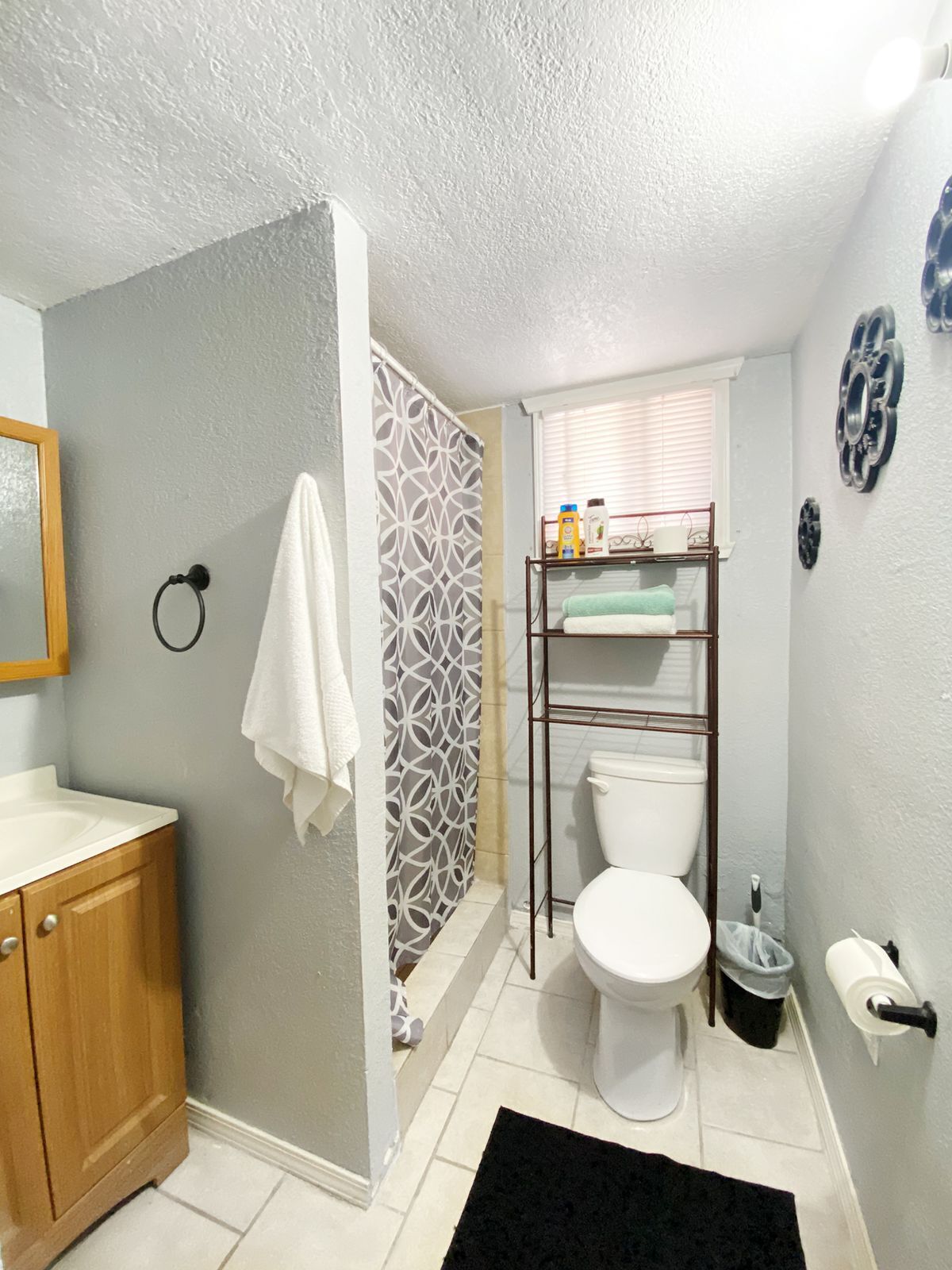 A bathroom with a wooden cabinet, a white sink, a toilet, a shower curtain, and a black rug.