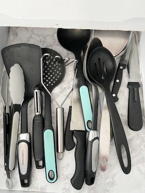 Un cassetto pieno di vari utensili da cucina, tra cui una spatola, una grattugia e un coltello.