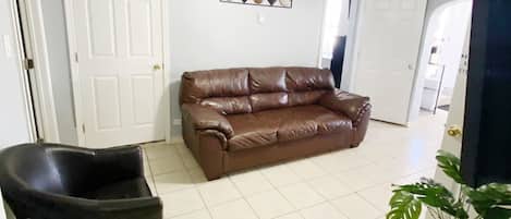 A living room with a brown leather sofa, a black armchair, a ceiling fan, and a decorative wall piece.