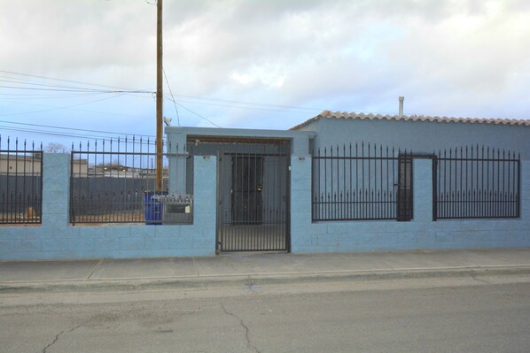 Un edificio azul con entrada protegida por una reja, una pequeña ventana y una valla metálica.