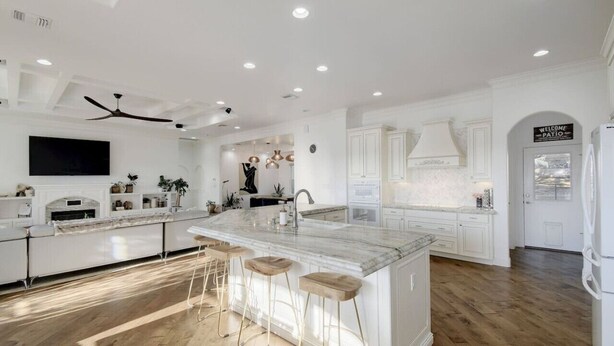 A modern kitchen with white cabinetry, a marble island with bar stools, and a ceiling fan. - 2 Luxury Homes | Group Retreats | Games | Fire Pit (Round Rock)