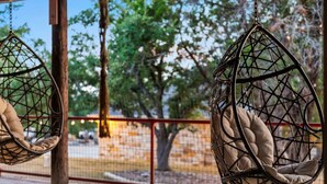 Two hanging chairs with cushions in an outdoor setting with a fence and trees in the background. - 2 Luxury Homes | Group Retreats | Games | Fire Pit (Round Rock)