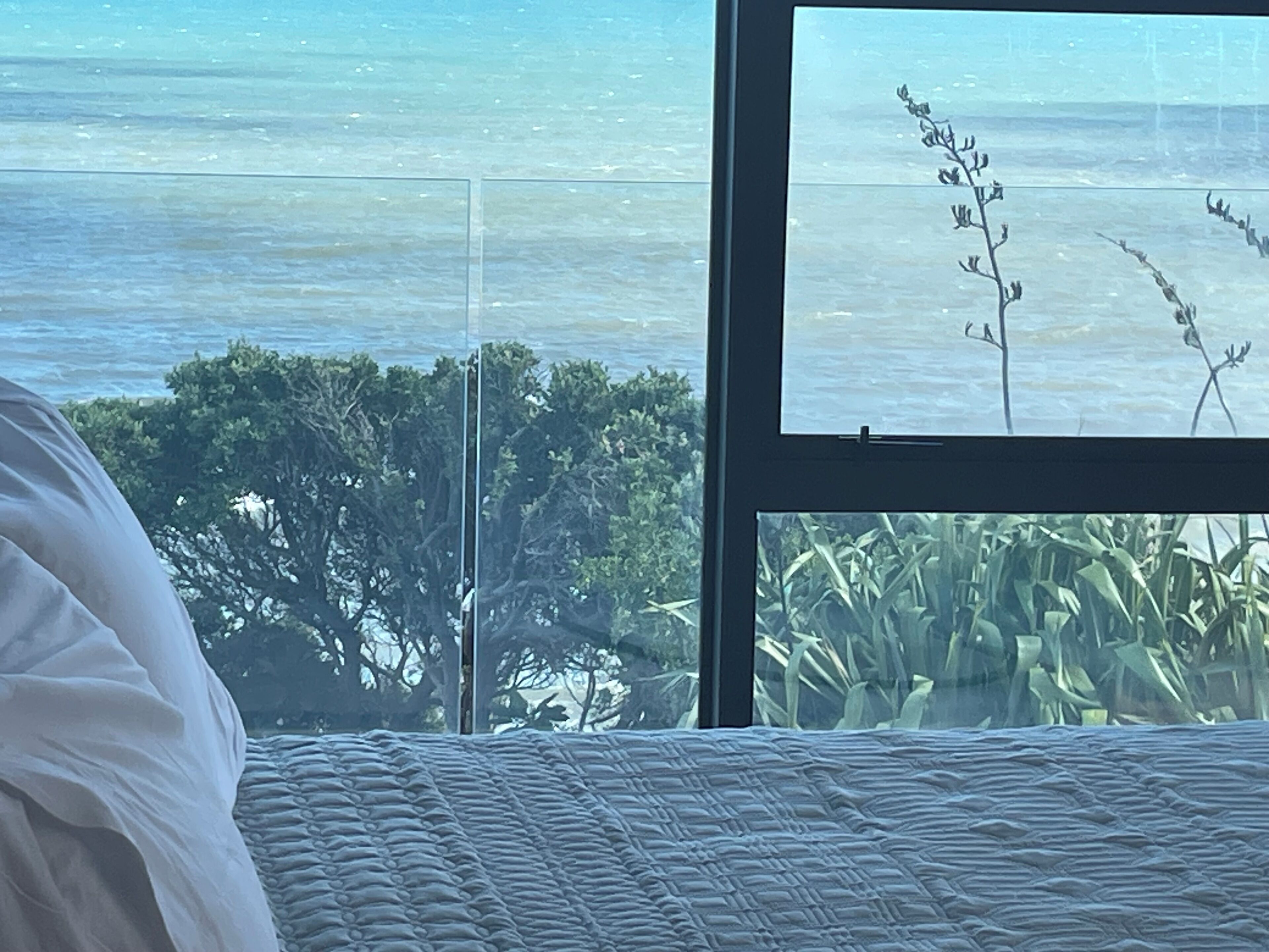 A bedroom with a large window overlooking a body of water and greenery.