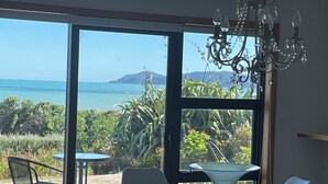 Un comedor con una mesa y sillas, una araña de cristal y vistas al mar y a las montañas a través de amplios ventanales.
