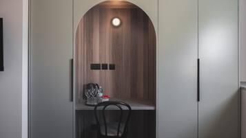 A compact kitchen area with a wooden accent wall, a small table with a kettle, glasses, and a bottle, and a black chair.