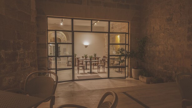 An interior space with a stone wall, a glass door leading to a dining area with tables and chairs, and a potted plant. - Maria Rosa Suites (Victoria)