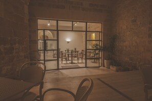 An interior space with a stone wall, a glass door leading to a dining area with tables and chairs, and a potted plant. - Maria Rosa Suites (Victoria)
