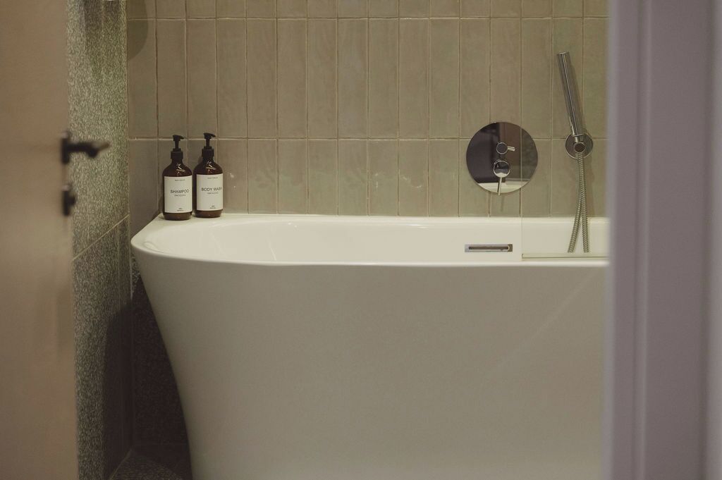 Un baño moderno con una bañera independiente, un cabezal de ducha manual y dos botellas de champú y gel de baño en un estante.