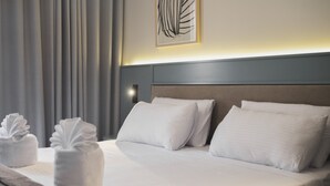A neatly made bed with white linens and pillows, a headboard with a light fixture, and a wall-mounted artwork. - Maria Rosa Suites (Victoria)