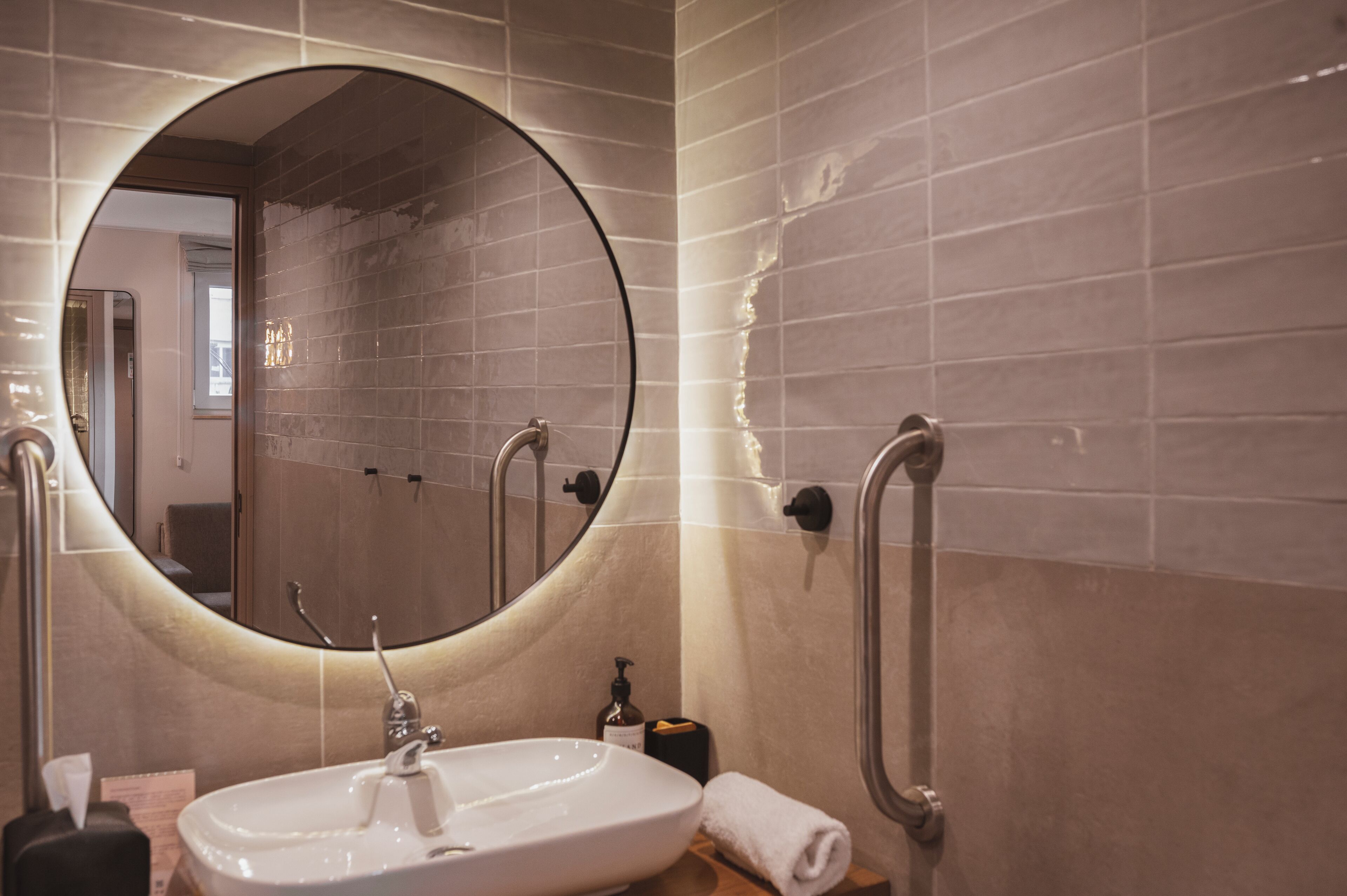 Une salle de bain avec un miroir rond, un lavabo et un porte-serviettes.