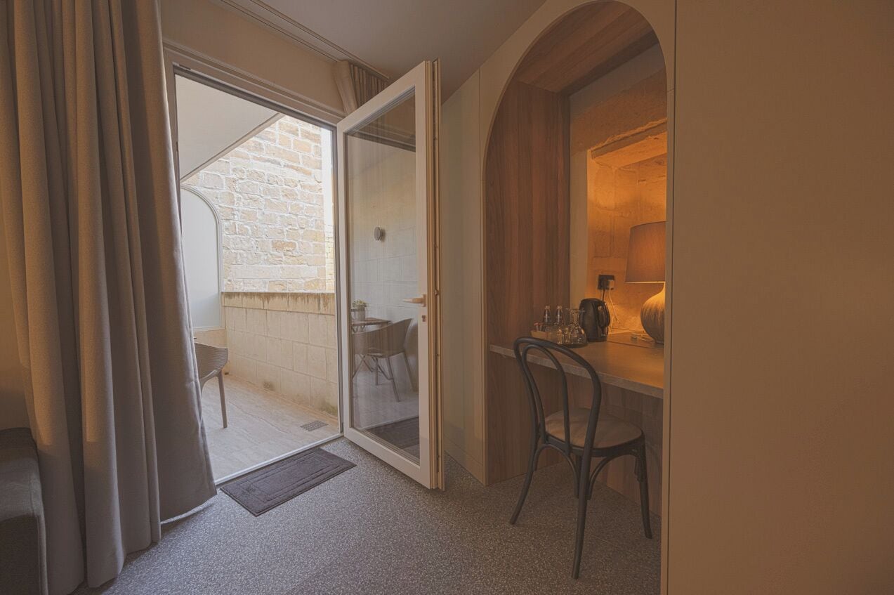 A room with a sliding glass door leading to an outdoor area with a stone wall and a table with chairs.