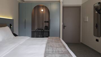 Ein Hotelzimmer mit Bett, Schreibtisch mit Stuhl, Spiegel und Tür.