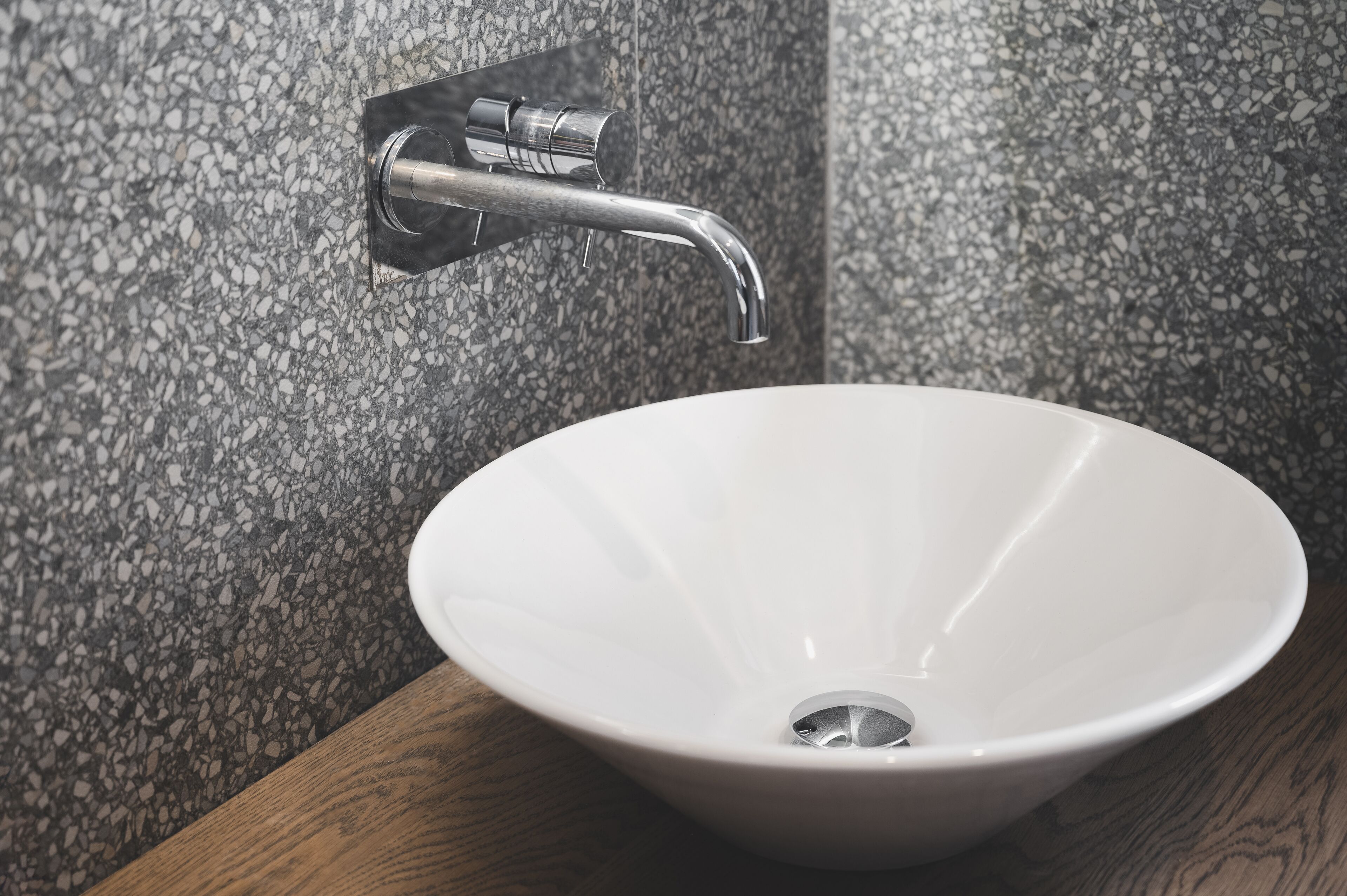 A bathroom with a white sink, a chrome faucet, and a speckled tile wall.