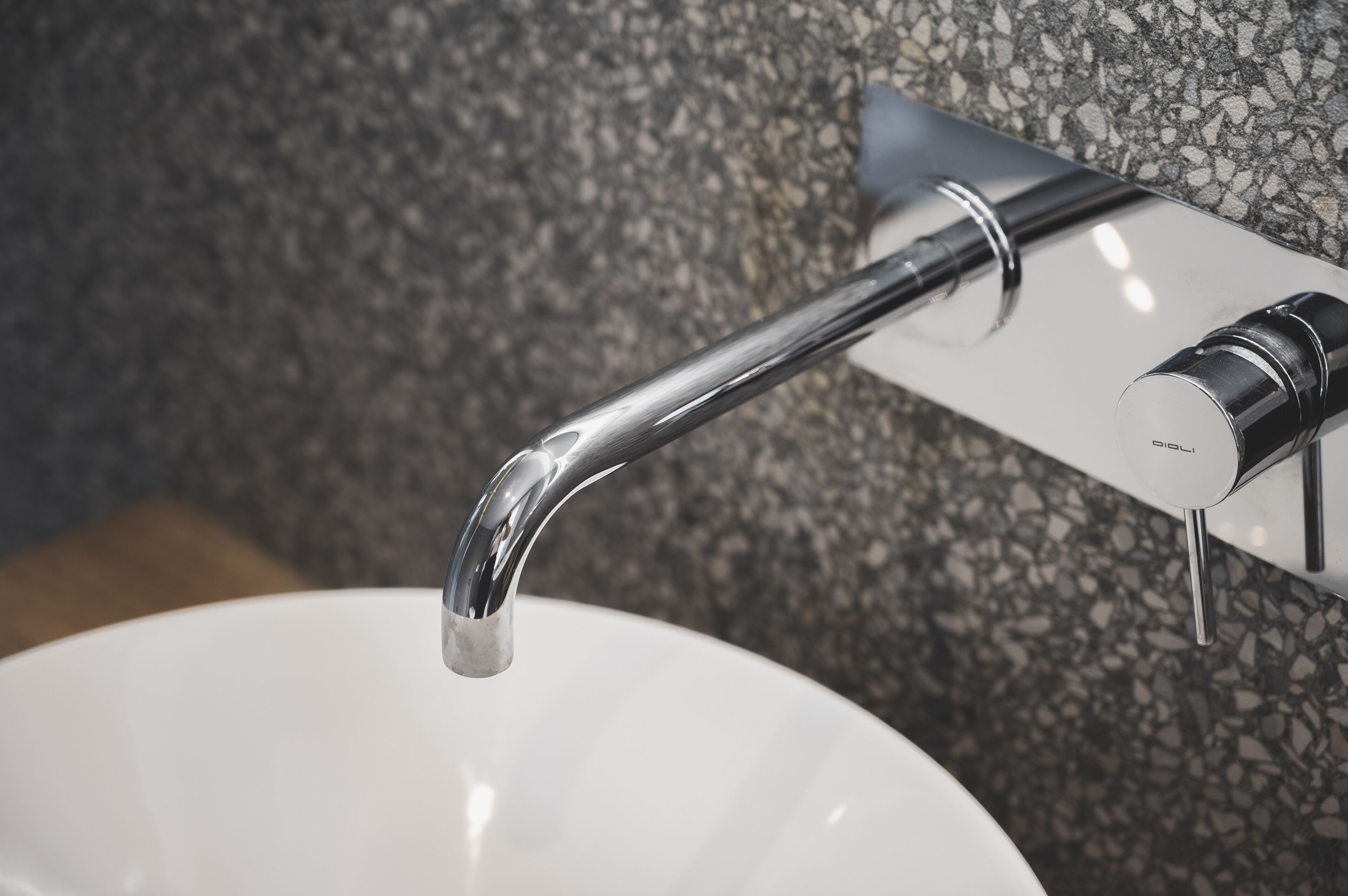 A modern bathroom with a chrome faucet and a white sink against a speckled granite wall.
