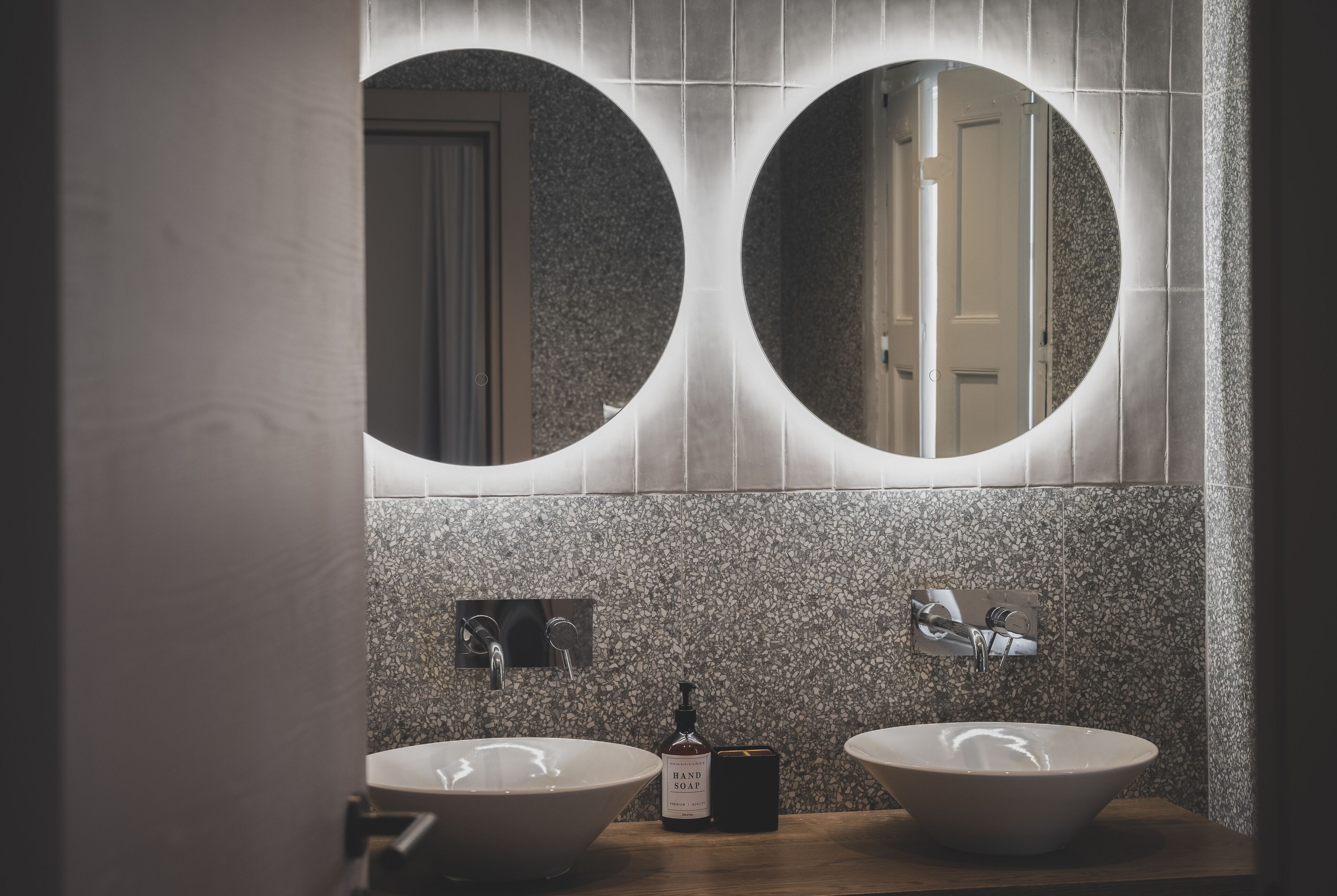 A bathroom with two round mirrors, a wooden vanity, and a bottle of hand soap.