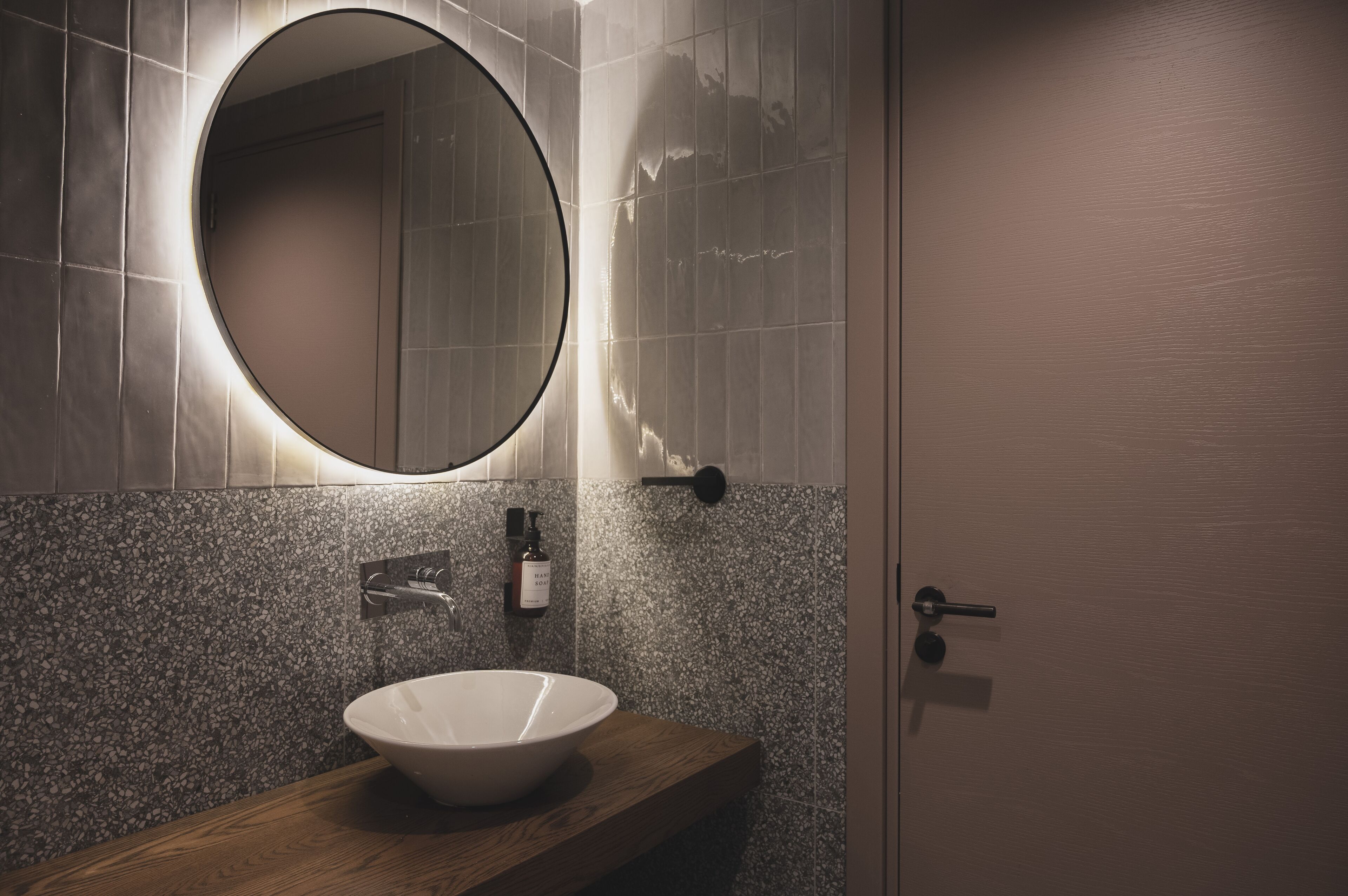 Un baño con un espejo redondo, un lavamanos blanco y una encimera de madera.