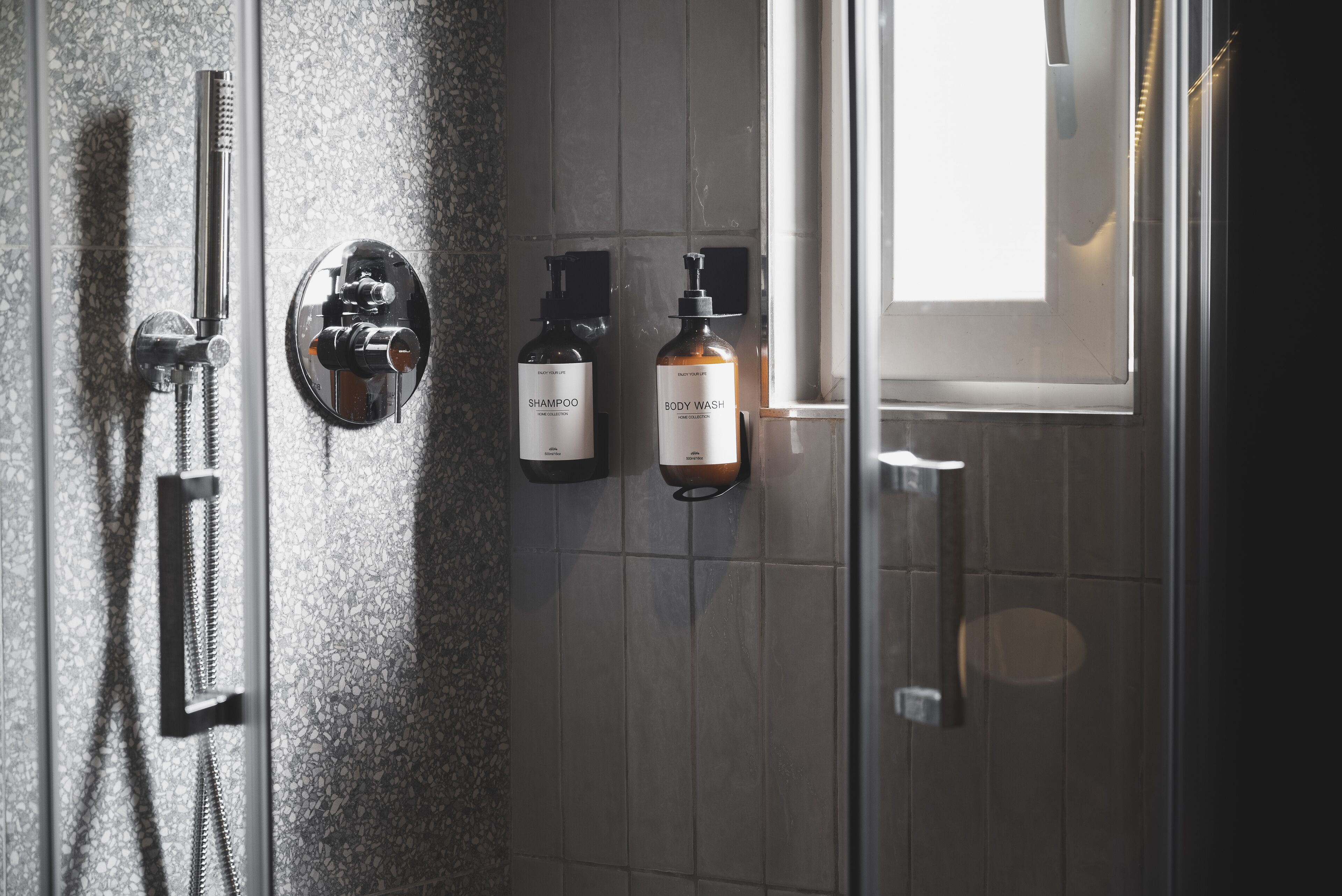 A bathroom with a shower, a toilet, and two bottles of shampoo and body wash on the wall.