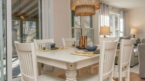 Un espace repas avec une table blanche, des chaises et un luminaire en fibres tressées.