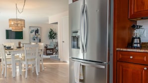 Une cuisine moderne dotée d’un réfrigérateur en acier inoxydable, de meubles en bois et d’un coin repas avec des chaises et une table blanches.