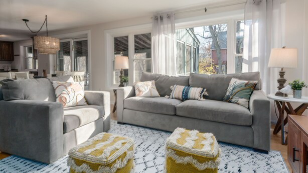 Un salon avec un canapé gris, deux fauteuils, un tapis à motifs et un lustre.