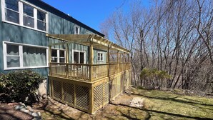 Une maison à deux étages avec une terrasse en bois et une cour clôturée.