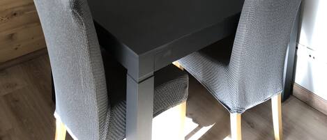 A modern dining area with a black table and grey upholstered chairs, wooden panel walls, and a white wall with a black abstract art piece.