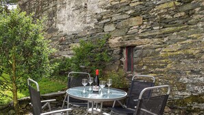 A stone wall with a small window, a round table with metal chairs, and a bottle of wine. - Church House Cottage (Ulpha)