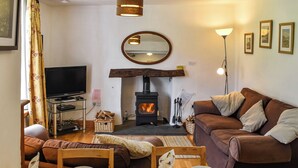 A cozy living room with a fireplace, a sofa, a television, and a dining table set for two. - Church House Cottage (Ulpha)