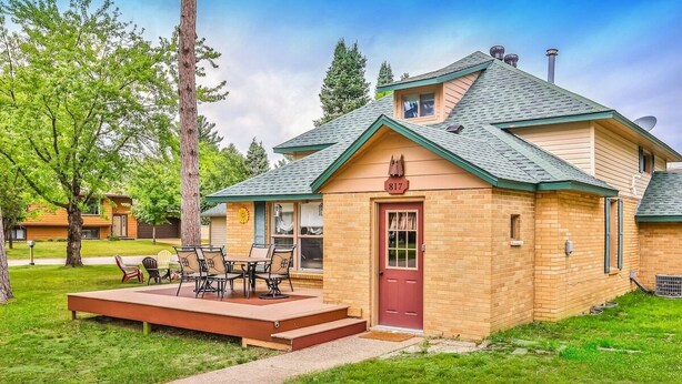 Una casa de un piso con puerta roja, un porche pequeño y una chimenea.