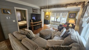 Una sala de estar acogedora con un sofá grande, un televisor y un comedor al fondo.