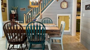 Un comedor con una mesa y sillas de madera, una escalera con barandillas azules y un reloj en la pared.