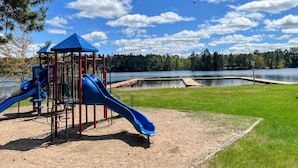 Un parque infantil con un tobogán azul y una estructura de escalada roja cerca de un lago.