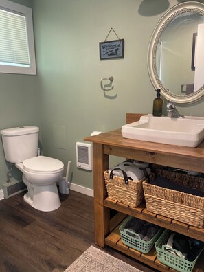 Une salle de bain équipée de toilettes, d’un lavabo avec un miroir, d’une étagère en osier et d’une pancarte de bienvenue.