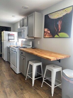 Una cocina con electrodomésticos blancos, encimera de madera y dos taburetes blancos.