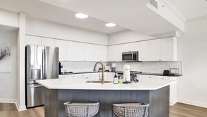 Una cocina moderna con armarios blancos, electrodomésticos de acero inoxidable y una isla central con taburetes de bar.