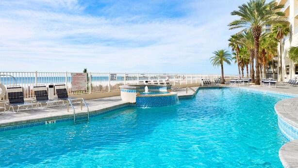 Piscina con sillones de descanso y palmeras, rodeada por una valla blanca.