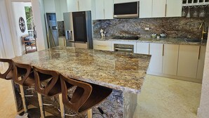 Eine moderne Küche mit Granitarbeitsplatte, Edelstahlgeräten und einer Bar mit Hockern.