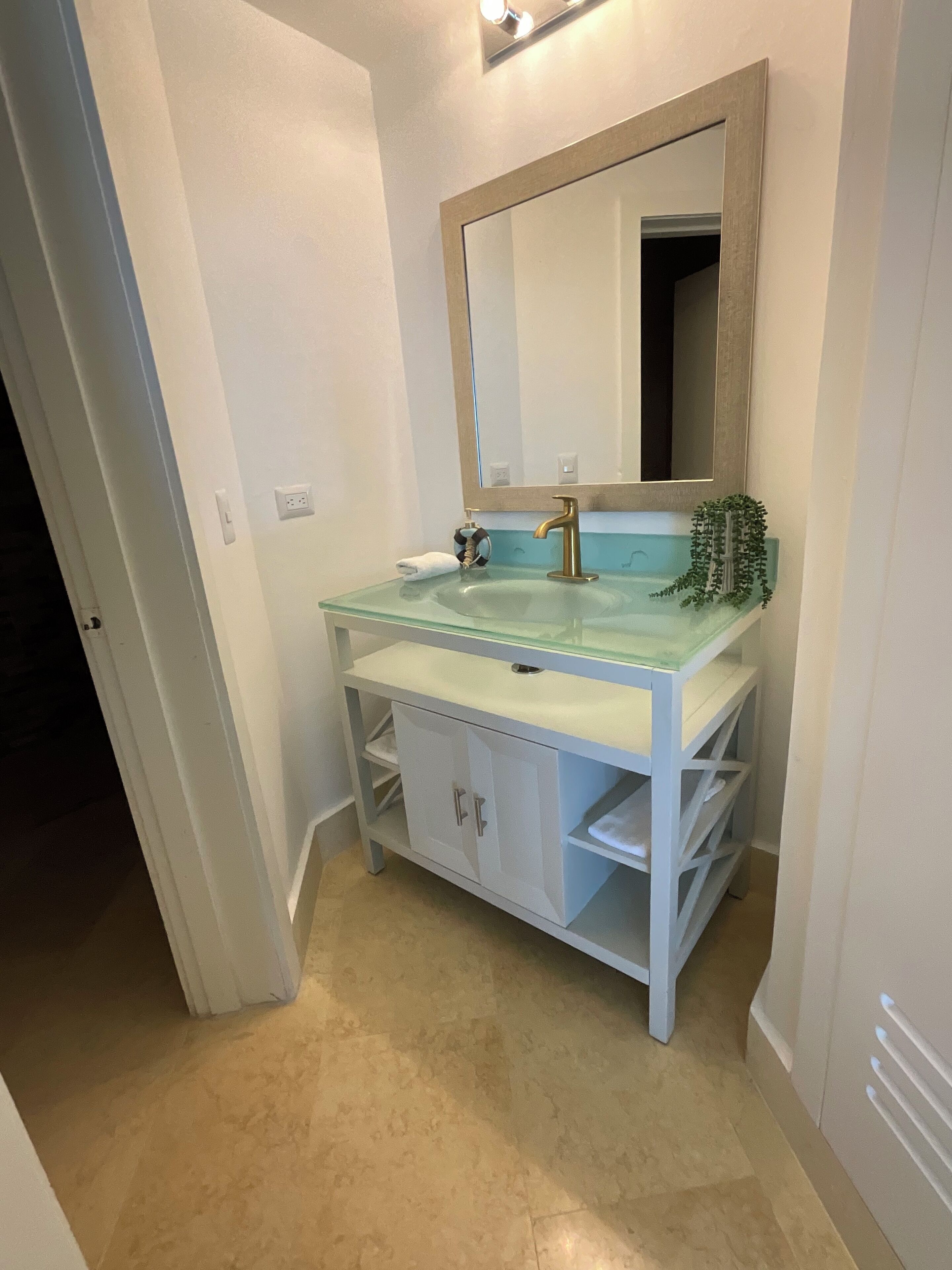 A bathroom with a glass sink, a gold faucet, a mirror, and a small plant.
