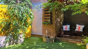 A small, well-maintained garden with artificial grass, a wooden fence, and two chairs with lobster-themed cushions.