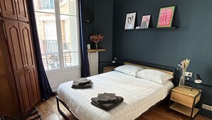 Ein Schlafzimmer mit Bett, Holzboden, Kleiderschrank, Nachttisch mit Lampe und einem Fenster mit Vorhängen.