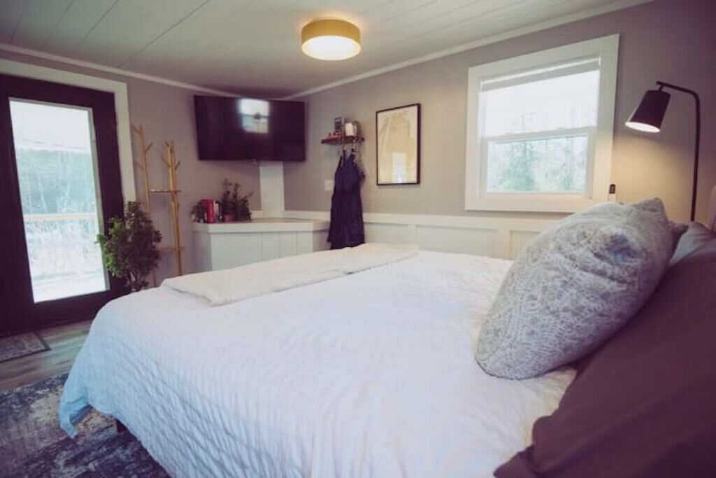 Ein Schlafzimmer mit einem Bett, einem an der Wand befestigten Fernseher, einem Fenster und einer Nachttischlampe.