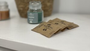 Un estante blanco con dos pequeños paquetes de papel marrón etiquetados “WELCOME Signature” y una pequeña botella azul.