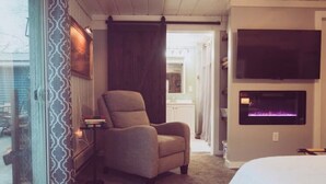 Una camera da letto con un letto grande, una poltrona, una TV a muro e un camino.