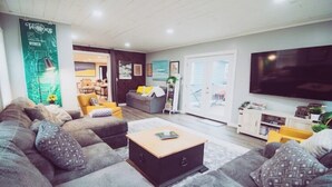Un soggiorno moderno con un divano grigio, un tavolino da caffè e una TV a schermo piatto. Sullo sfondo, una zona pranzo con sedie gialle.