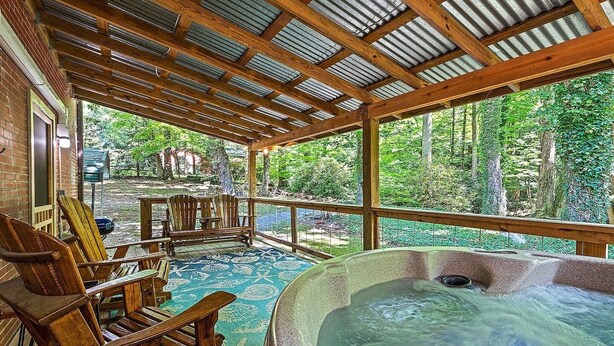 Une terrasse en bois avec un jacuzzi, des chaises et une vue sur une forêt.
