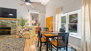 Un salon doté d’une cheminée en pierre, d’une table à manger avec des chaises, d’un ventilateur de plafond et d’une grande fenêtre avec des rideaux.