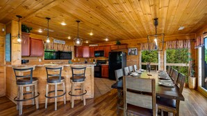 A wooden cabin interior with a kitchen, dining area, and bar. - Summer Starts Here + Breathtaking Views (Pigeon Forge)