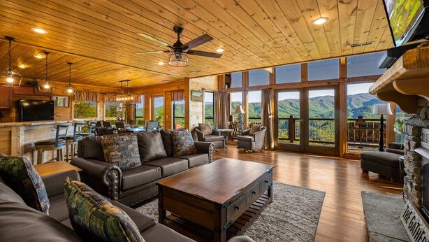 A spacious living area with a large wooden ceiling, leather sofas, a coffee table, and a stone fireplace. - Summer Starts Here + Breathtaking Views (Pigeon Forge)